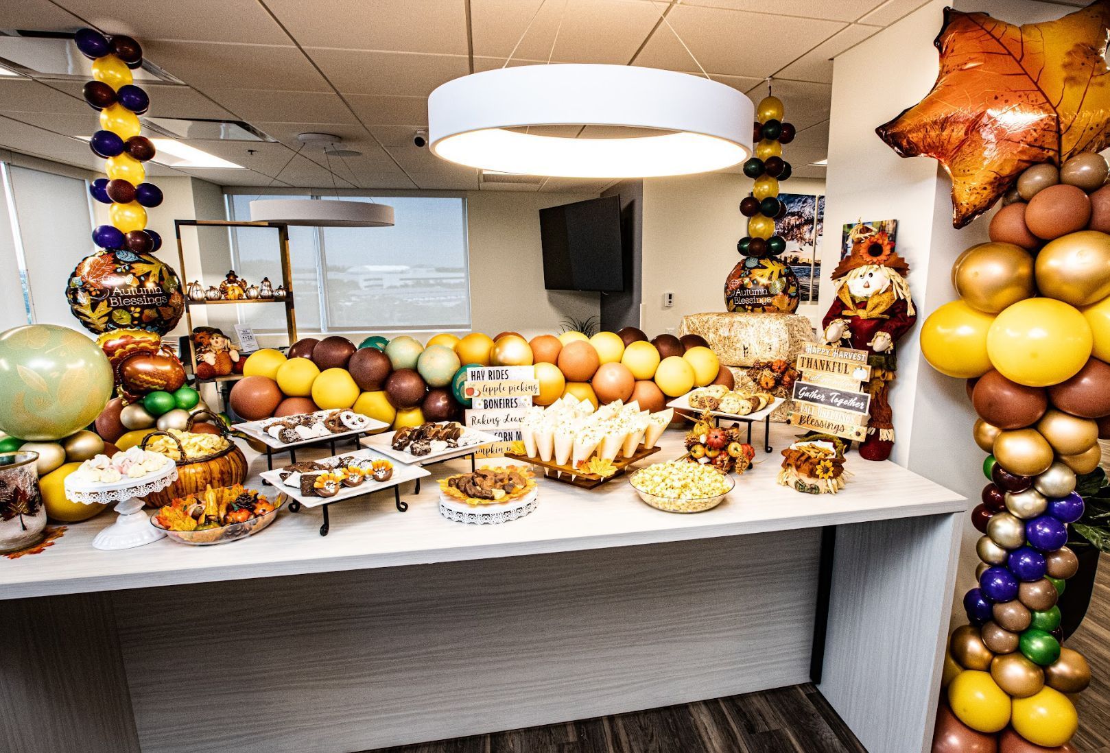 A beautifully decorated food count for the Fall.  There is a fall inspired balloon column, popcorn display, scarecrow and balloon chandeliers.