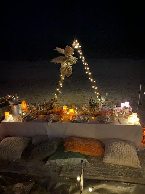 A beach side set up to celebrate a birthday, the wood triagle piece featured lights and a bo ho flower boutiquet. The low to the ground table was filled with flowers, candles and lush pillows for comfort. Hallandale Beach in the spring by An Elegant Picnic.