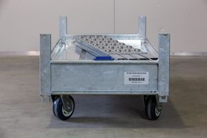 A metal cart with wheels is sitting on the floor in a warehouse.