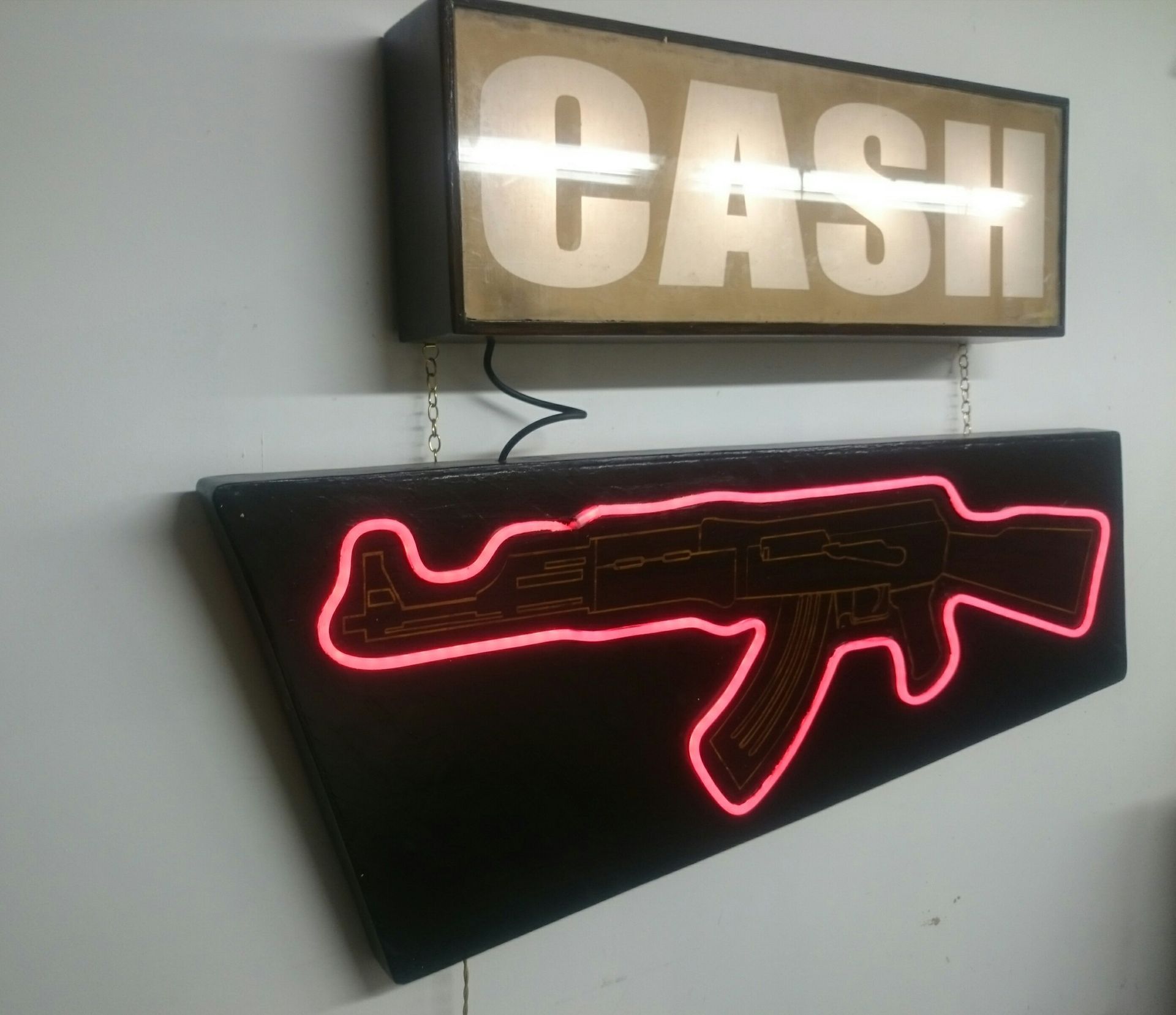 A neon looking sign of a gun below a light up box reading cash. By Matt Sargent.t