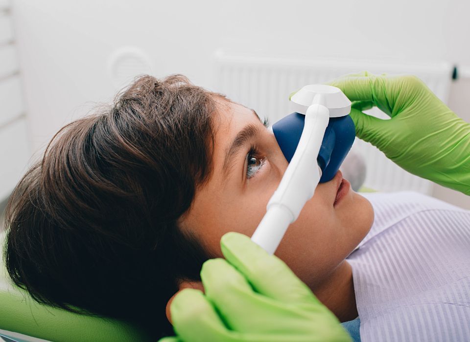 Child receiving gas anesthesia at the dentist, blue mask held by gloved hands.