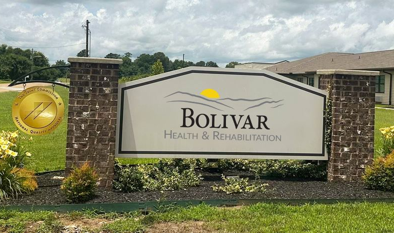 Sign for Bolivar Health & Rehabilitation with logo, brick columns, grass, and building in background.