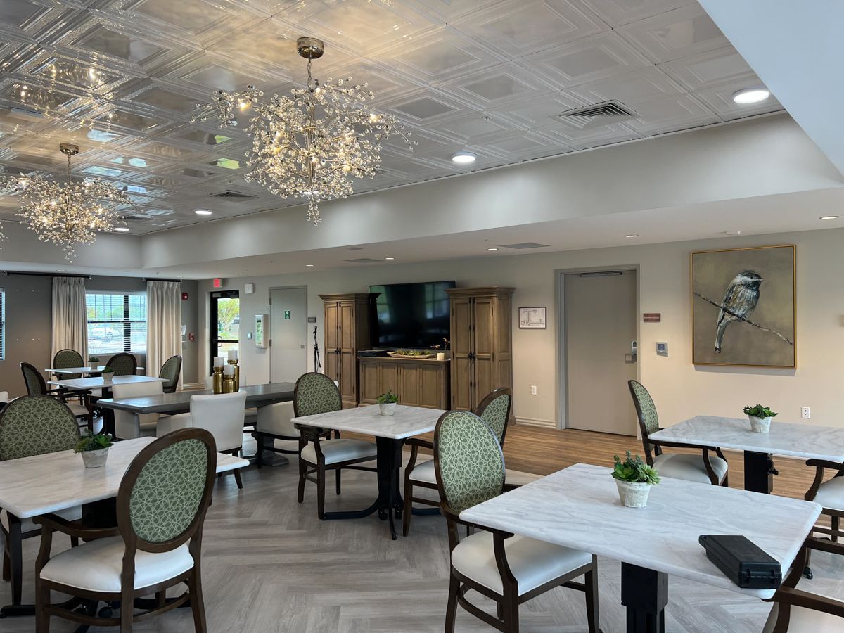 Dining room with tables, chairs, and chandeliers. Neutral tones, artwork on wall.