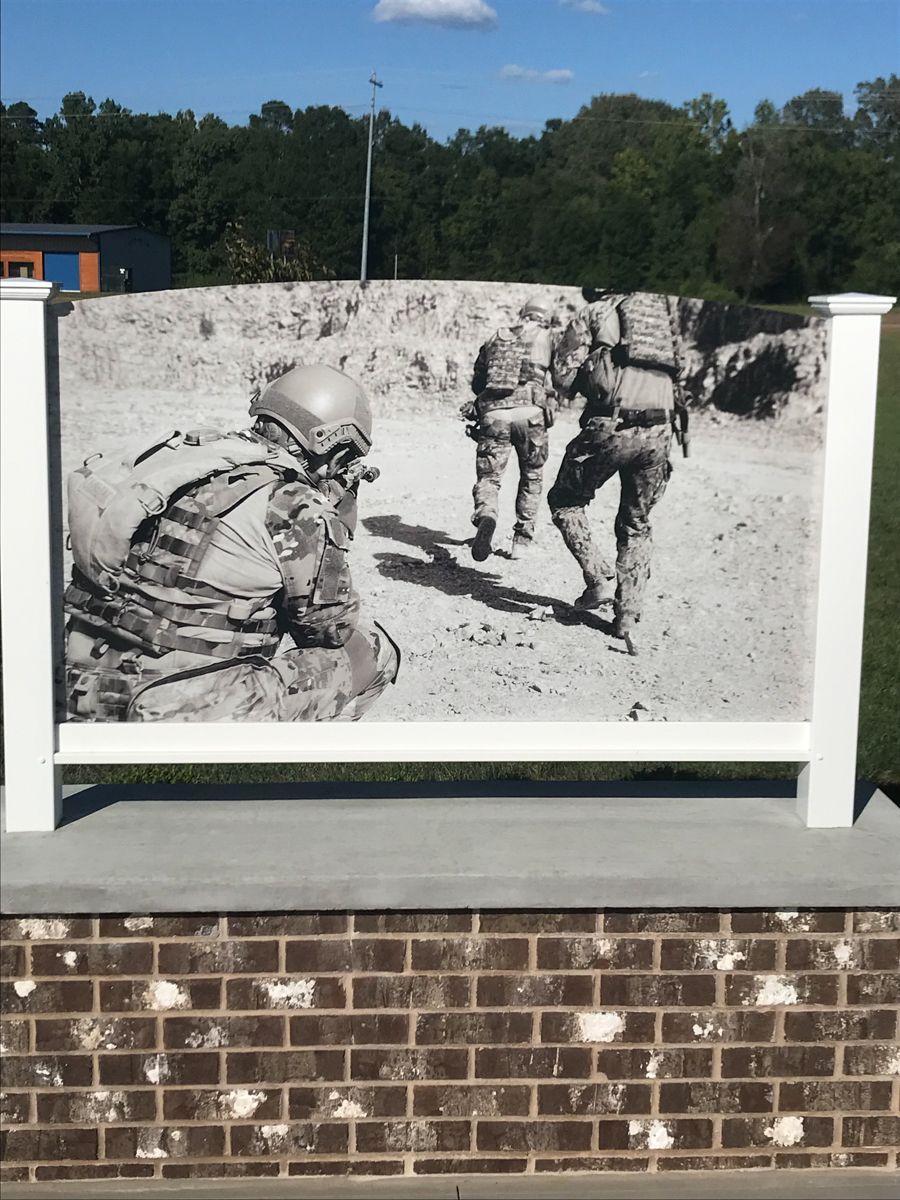 Black and white mural of soldiers in combat gear, set on brick and concrete with white pillars; outdoors.
