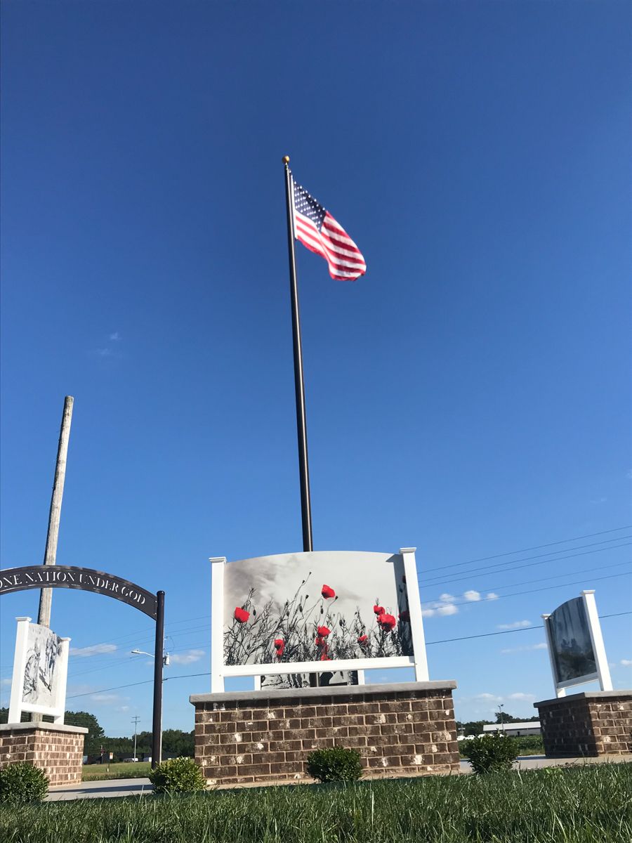 American flag waves over a memorial with poppy artwork against a clear blue sky.