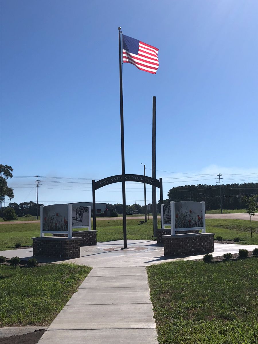 A memorial with a waving American flag. Two display cases flank a central arch; blue sky above.