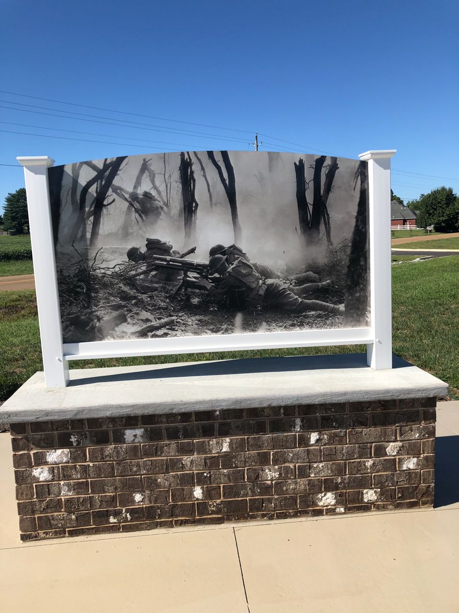 Memorial display with a black and white war photograph. The display is supported by a brick base and a white frame.