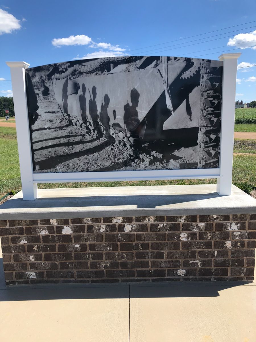 Monument with a black and white photo of people near train tracks, set against a brick base and blue sky.