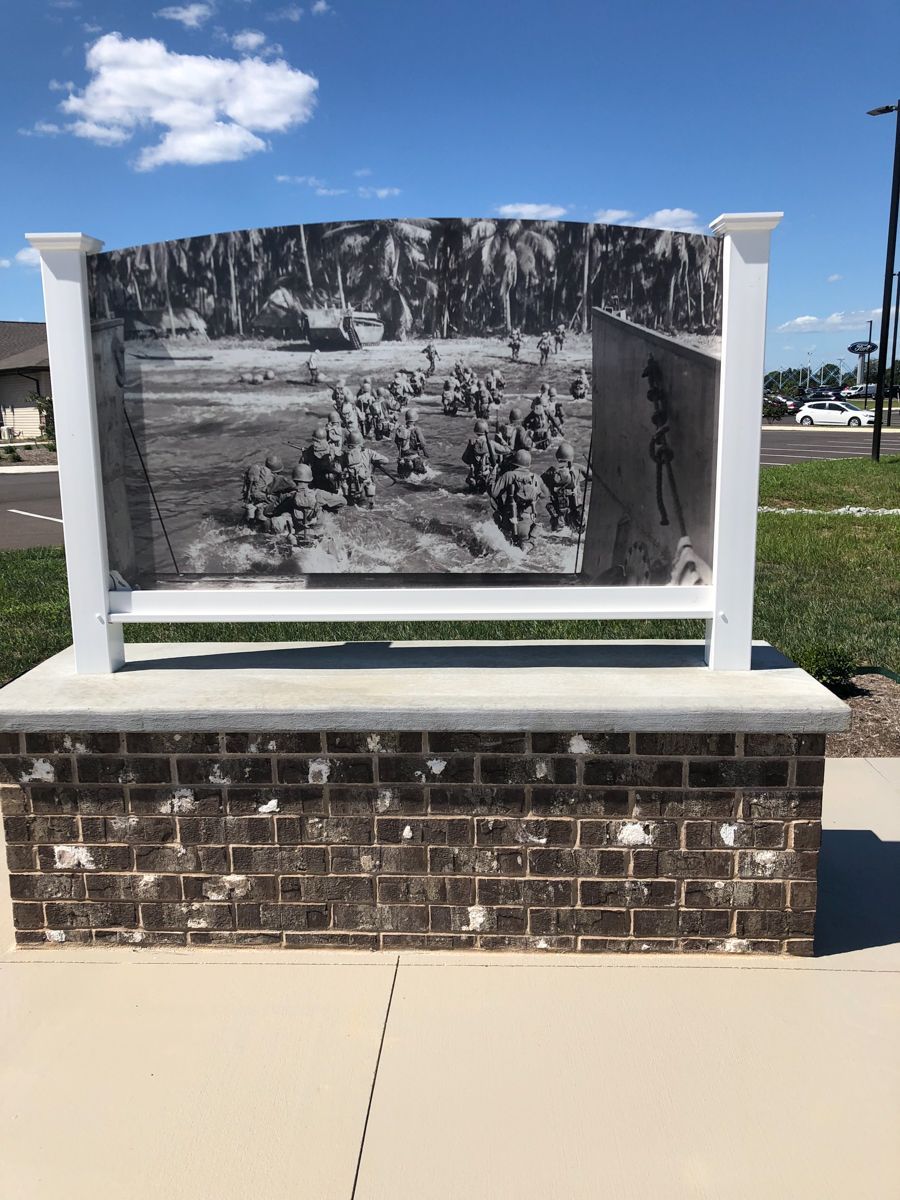 Historical photo display: Black and white image of people outdoors, in a park-like setting, mounted on brick and white posts.