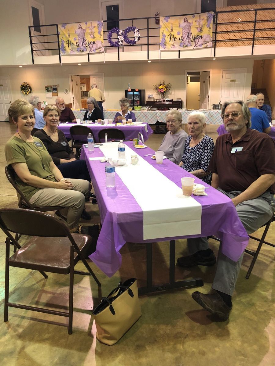 People seated at tables with purple tablecloths at an event in a large hall.
