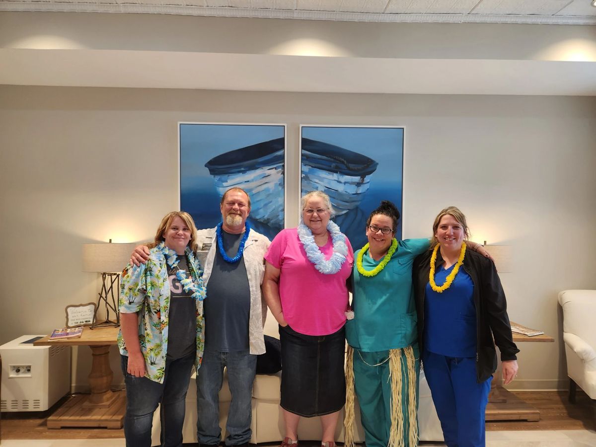 Five people smiling, wearing leis. Standing in front of blue artwork in a room.