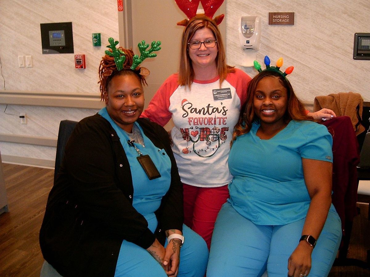Three healthcare workers with reindeer antlers, smiling, in a room.