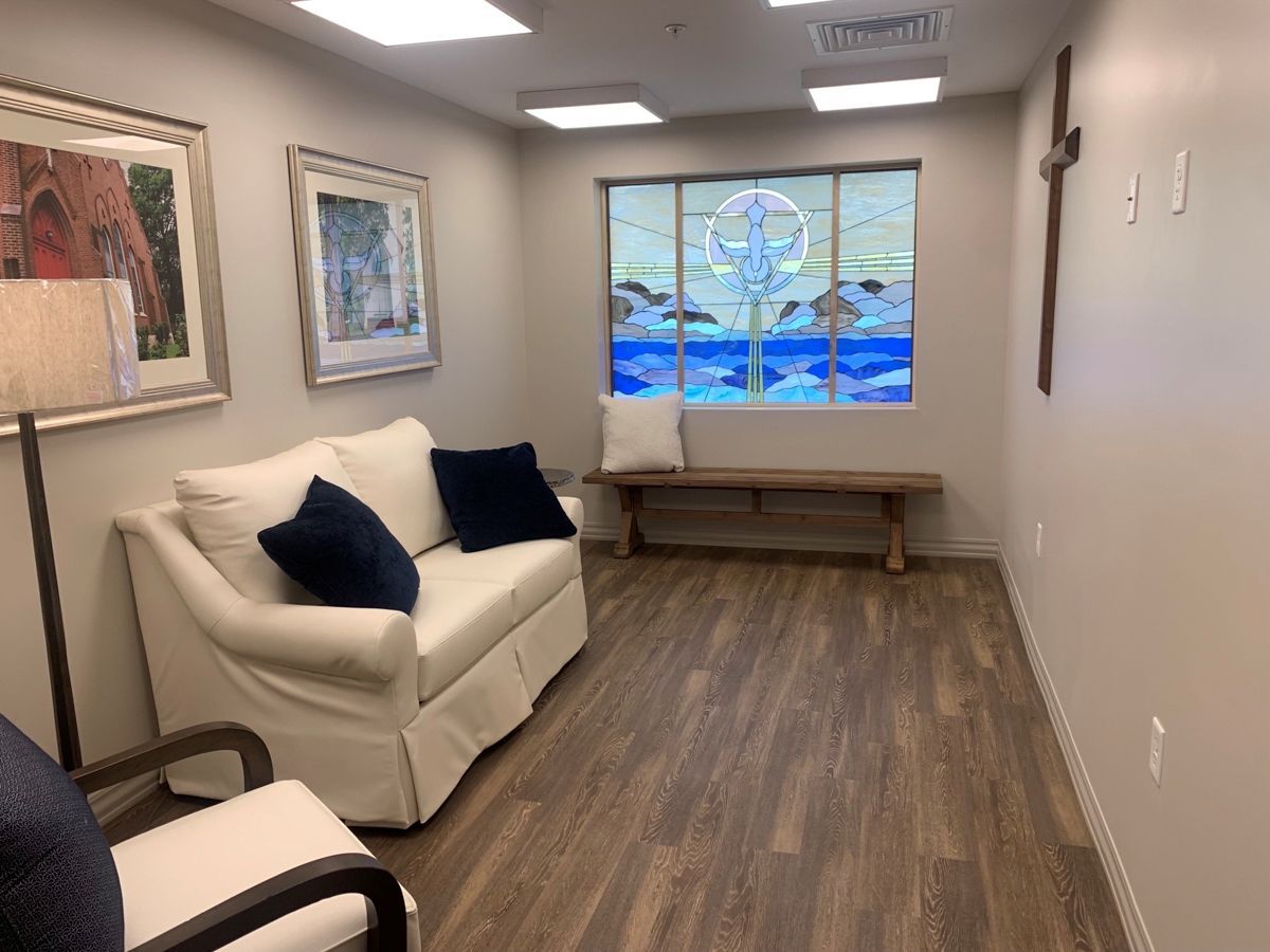 Cozy room with couch, chair, wooden bench, stained glass window, artwork, and a cross on the wall.