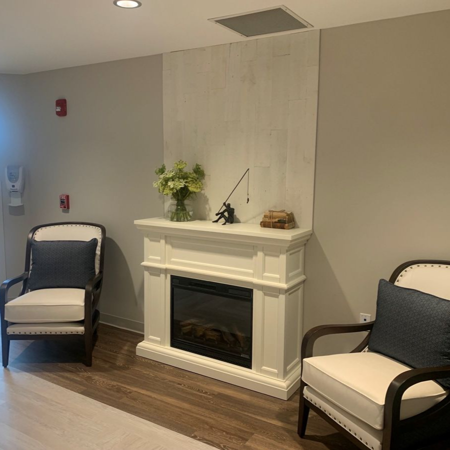 Two armchairs face a white fireplace with décor in a waiting room.