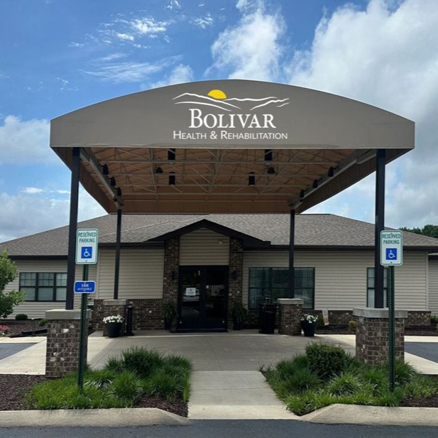Entrance to Bolivar Health & Rehab facility, tan awning, stone pillars, accessible parking signs, blue sky.