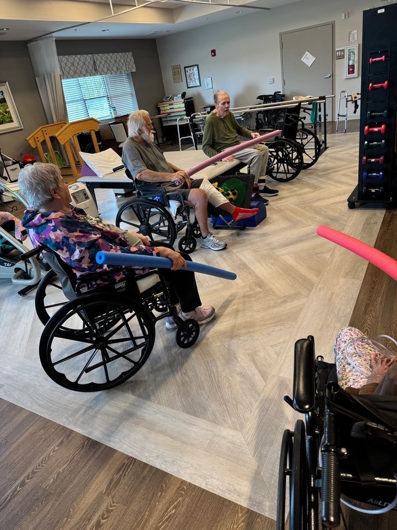 People in wheelchairs exercising with foam rollers in a senior center gym.