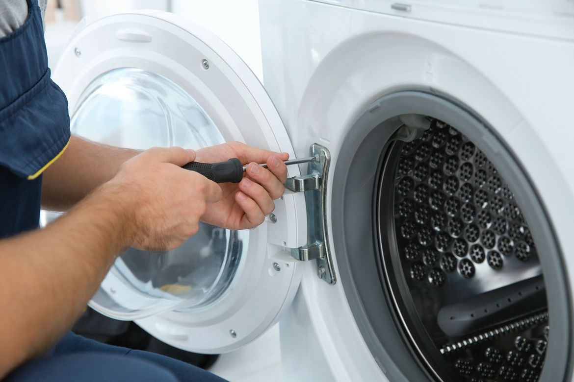 A man is fixing a washing machine with a screwdriver.