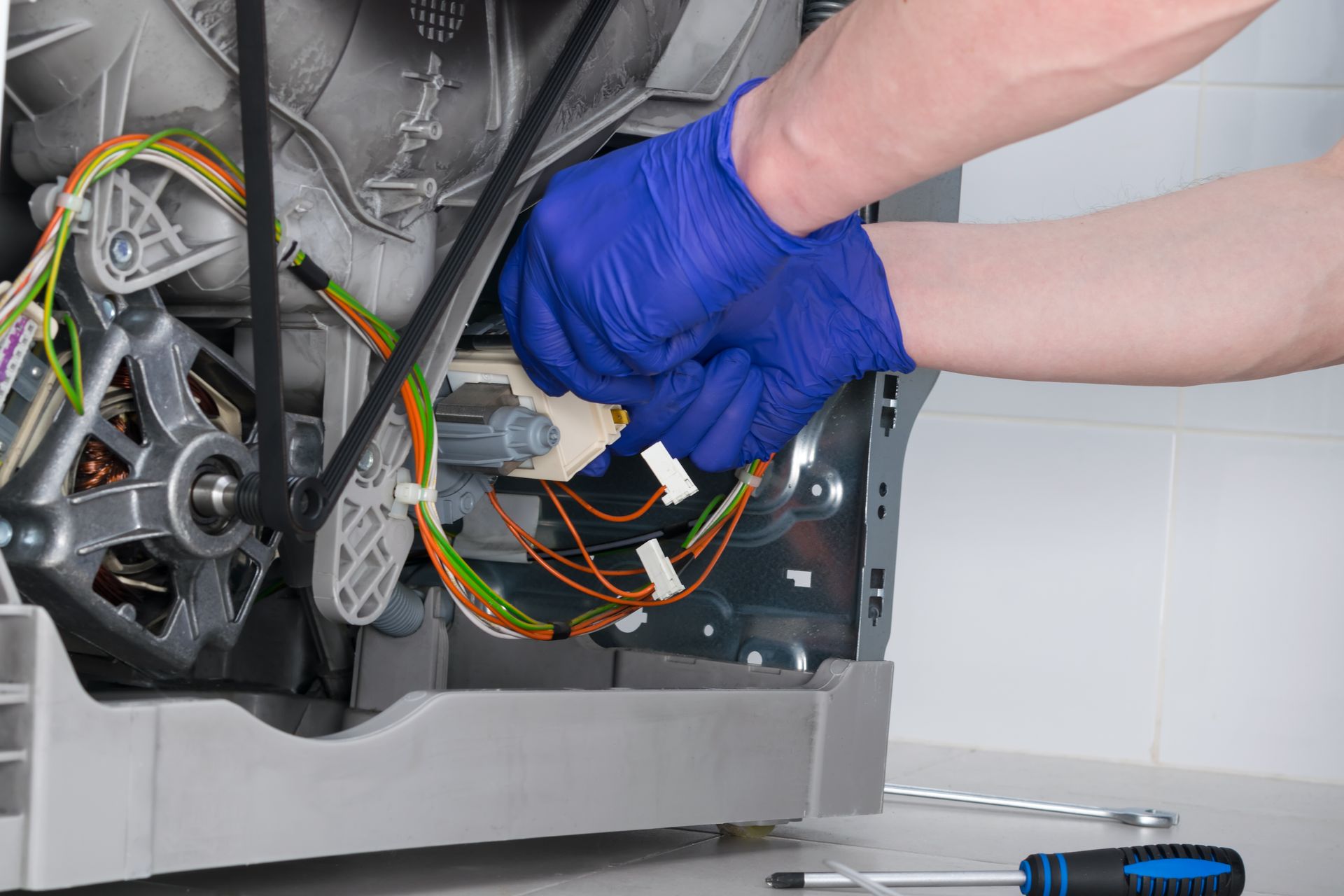 A person wearing blue gloves is working on a washing machine.