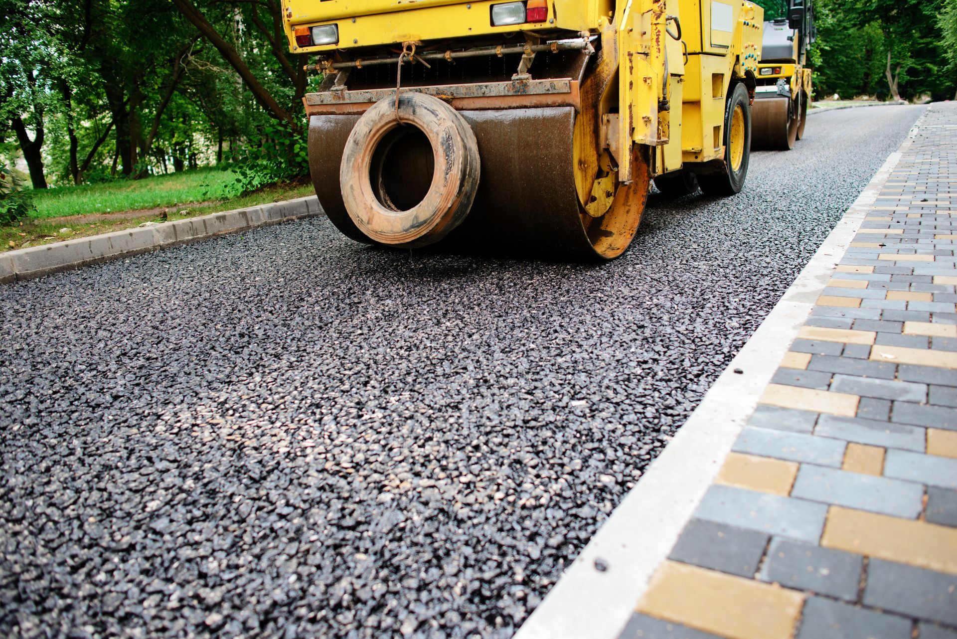 Road roller paving fresh asphalt beside a tiled sidewalk