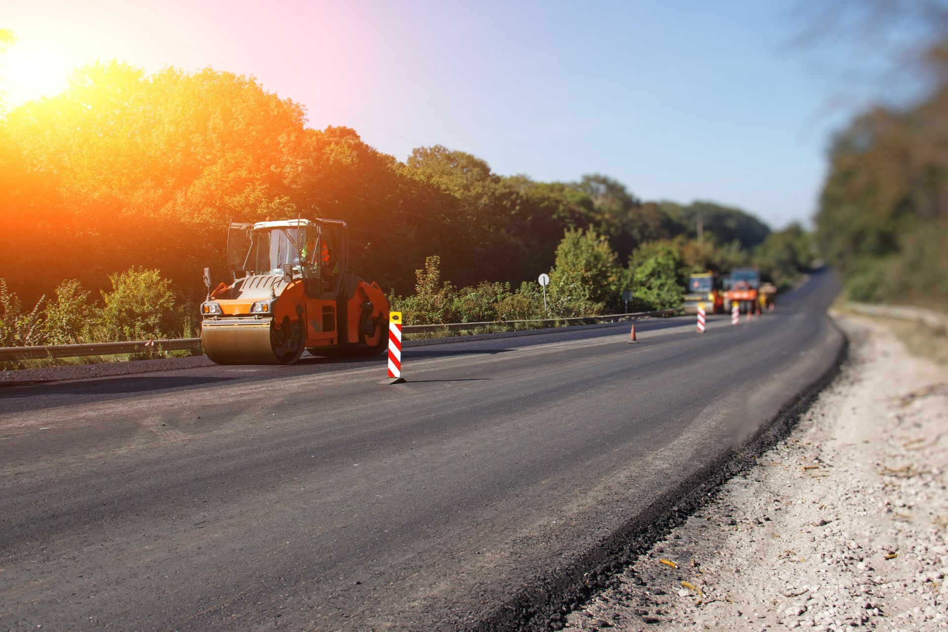 Road construction crew with rollers and traffic cones on a sunlit asphalt road in a rural area