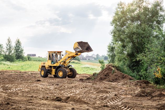 Yellow front loader moving dirt at a construction site beside trees and open field