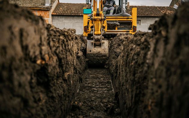Yellow excavator digging a trench between tall dirt walls in a construction site