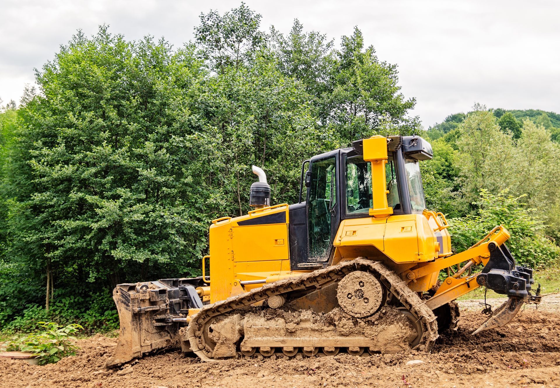 Yellow bulldozer at a muddy worksite with trees in the background