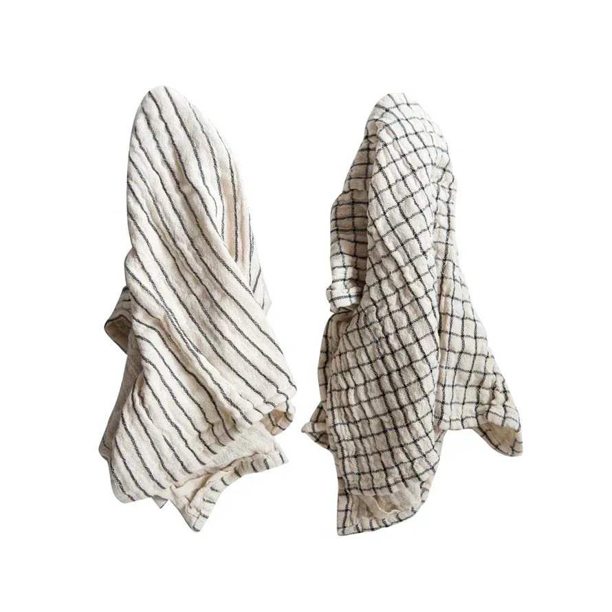 Two towels , one striped and one checkered , are hanging on a white background.