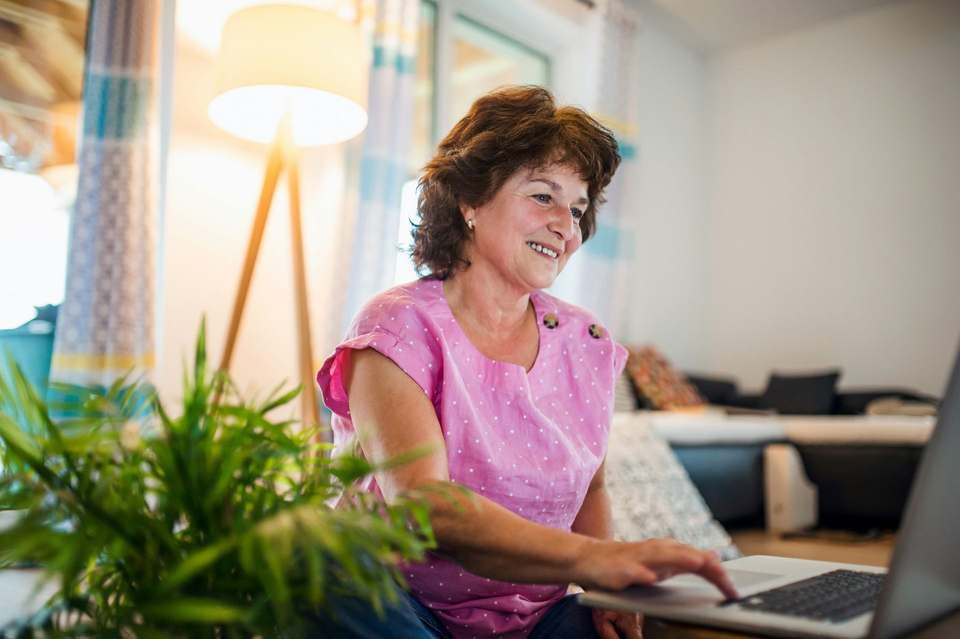 Woman in pink shirt smiles while using a laptop indoors.