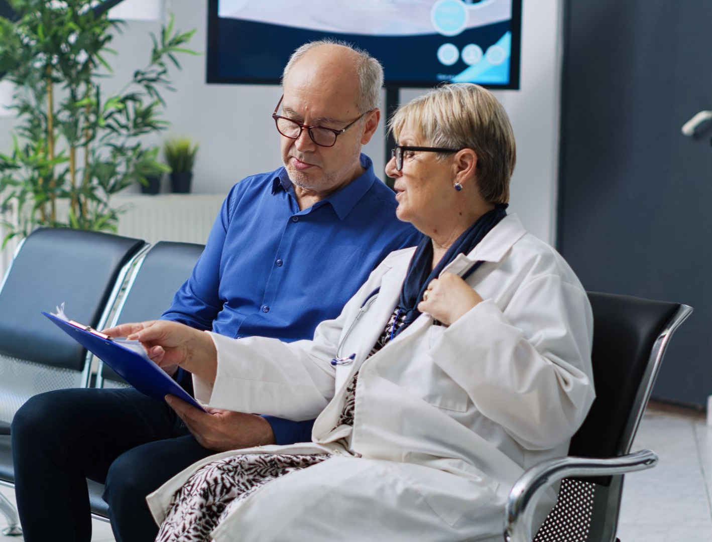 Doctor showing patient a document in a waiting room, both wearing glasses.