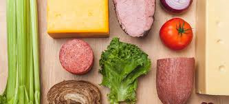 Arrangement of sandwich ingredients: cheese, meat, salami, tomato, onion, lettuce, bread, celery, and more cheese.