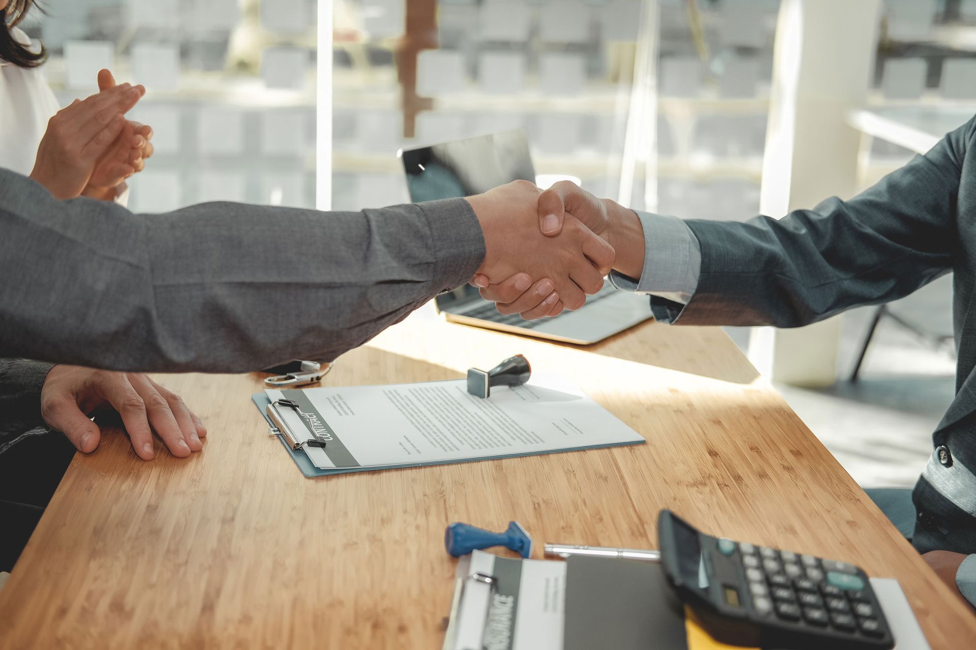 Two men are shaking hands over a wooden table.