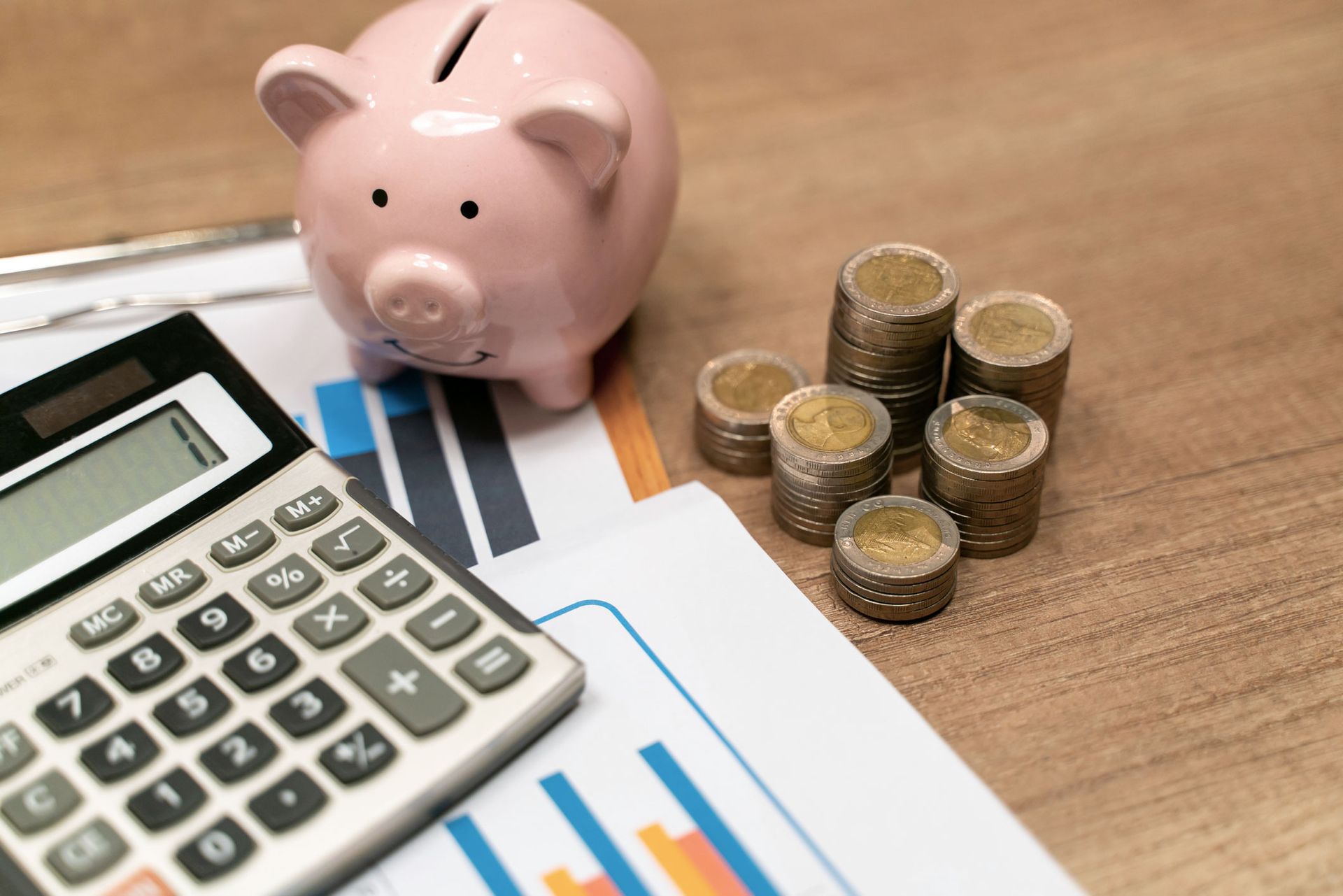 A piggy bank , a calculator , and stacks of coins on a table.