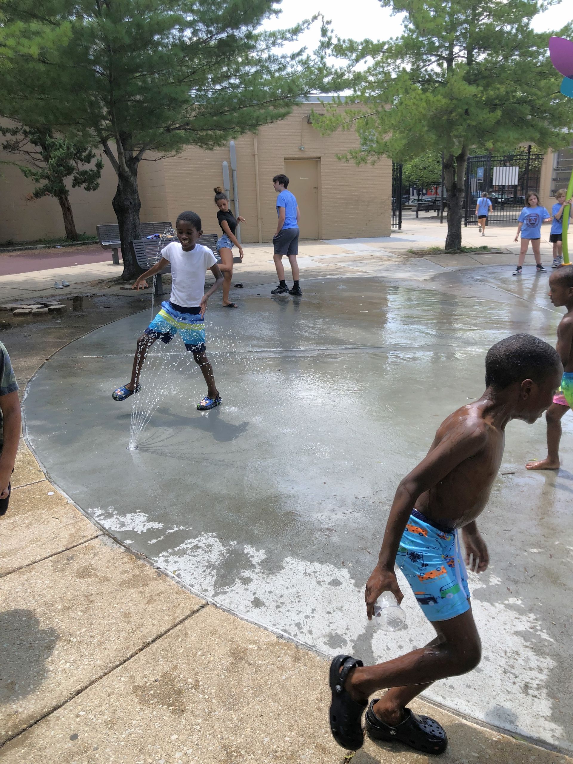 Children playing in a splash pad, sunny day. One is mid-air, another running.