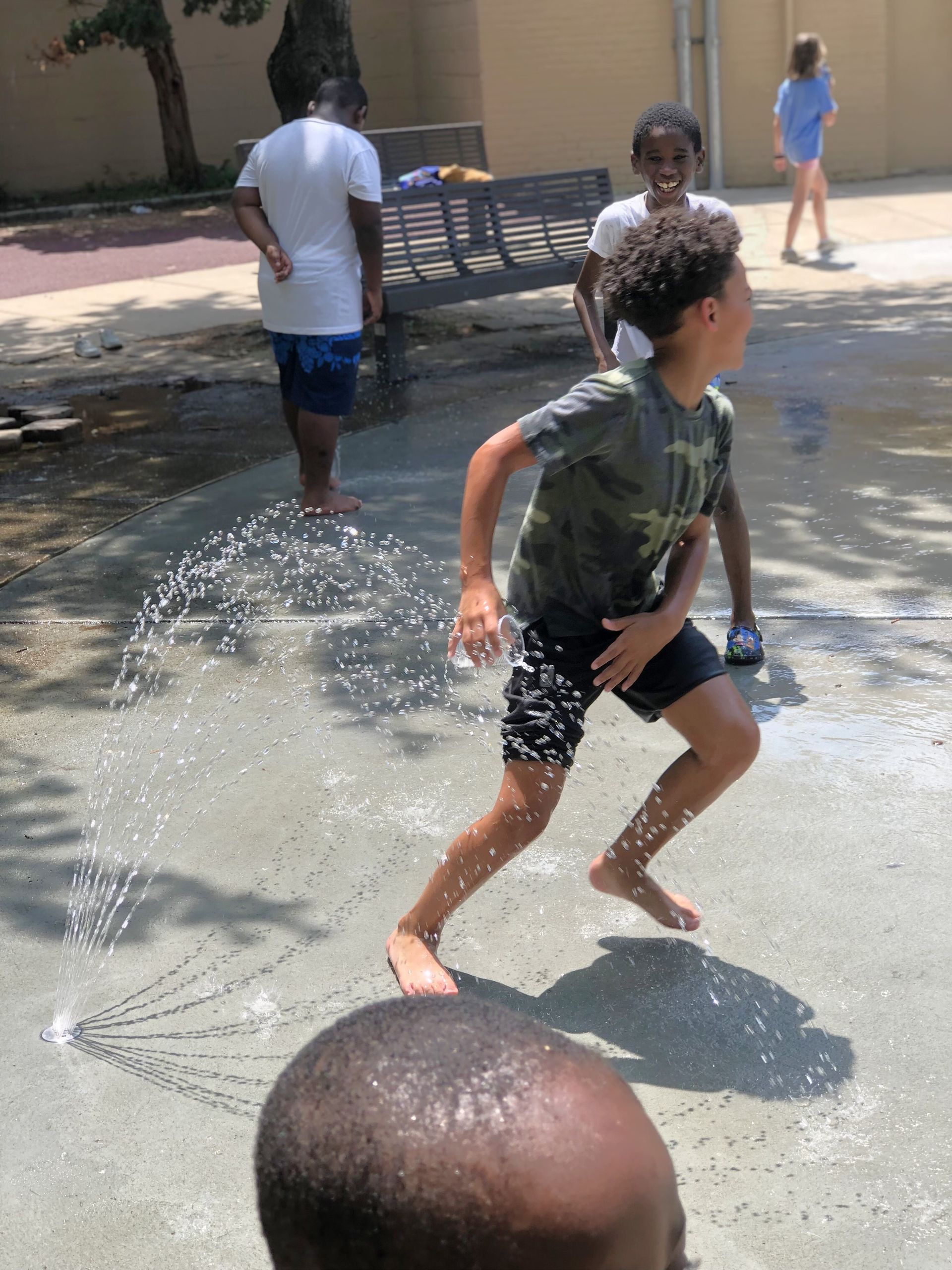 Children playing in a water fountain on a sunny day, laughing and running.