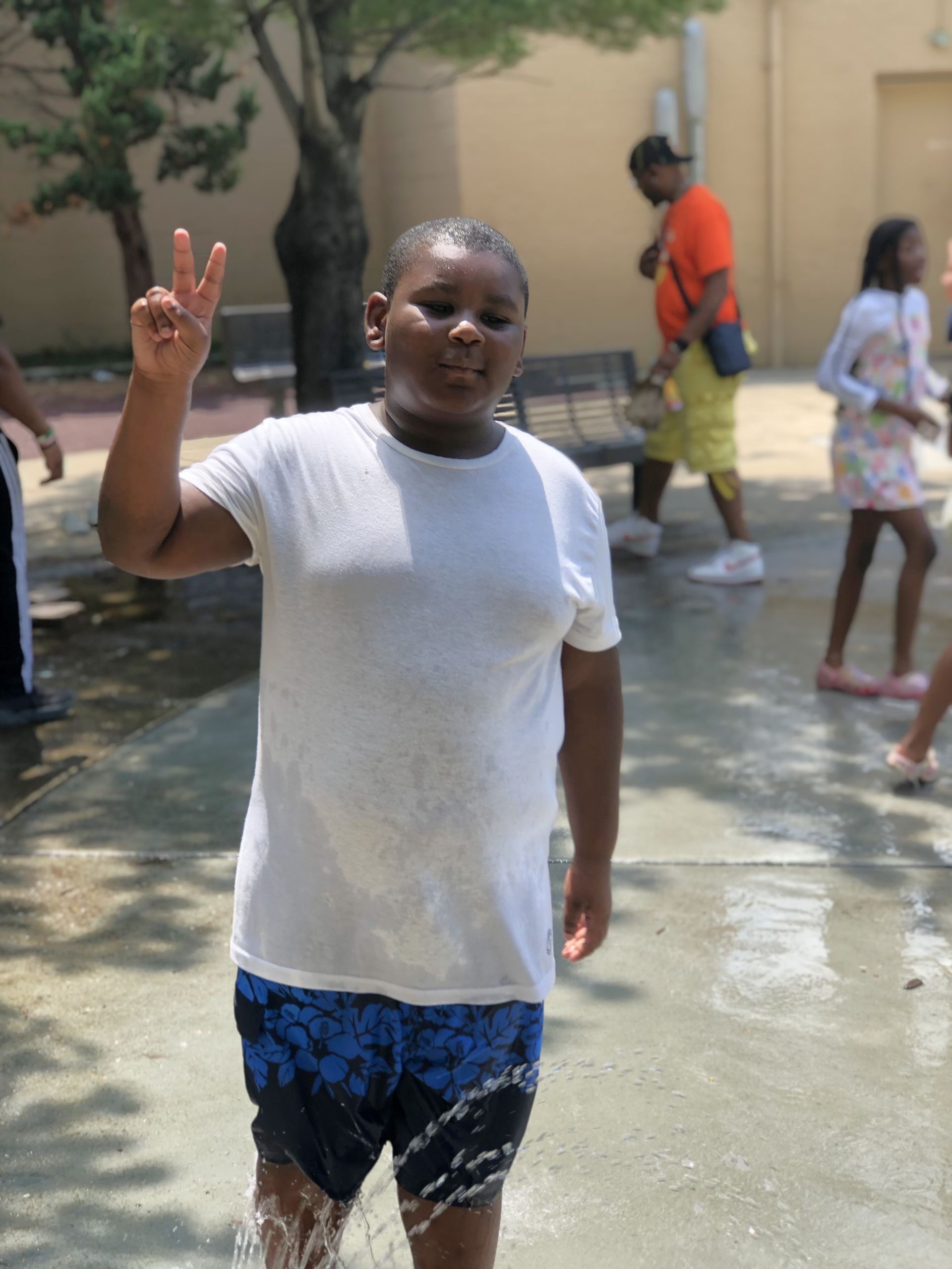 Boy in wet clothes gives peace sign outdoors.