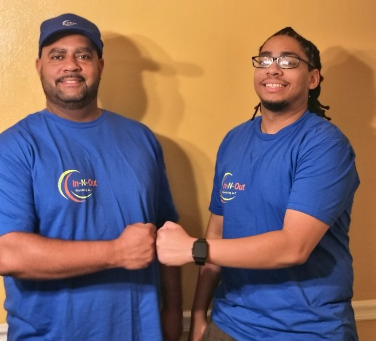 Two people in blue shirts fist-bump in front of a yellow wall.
