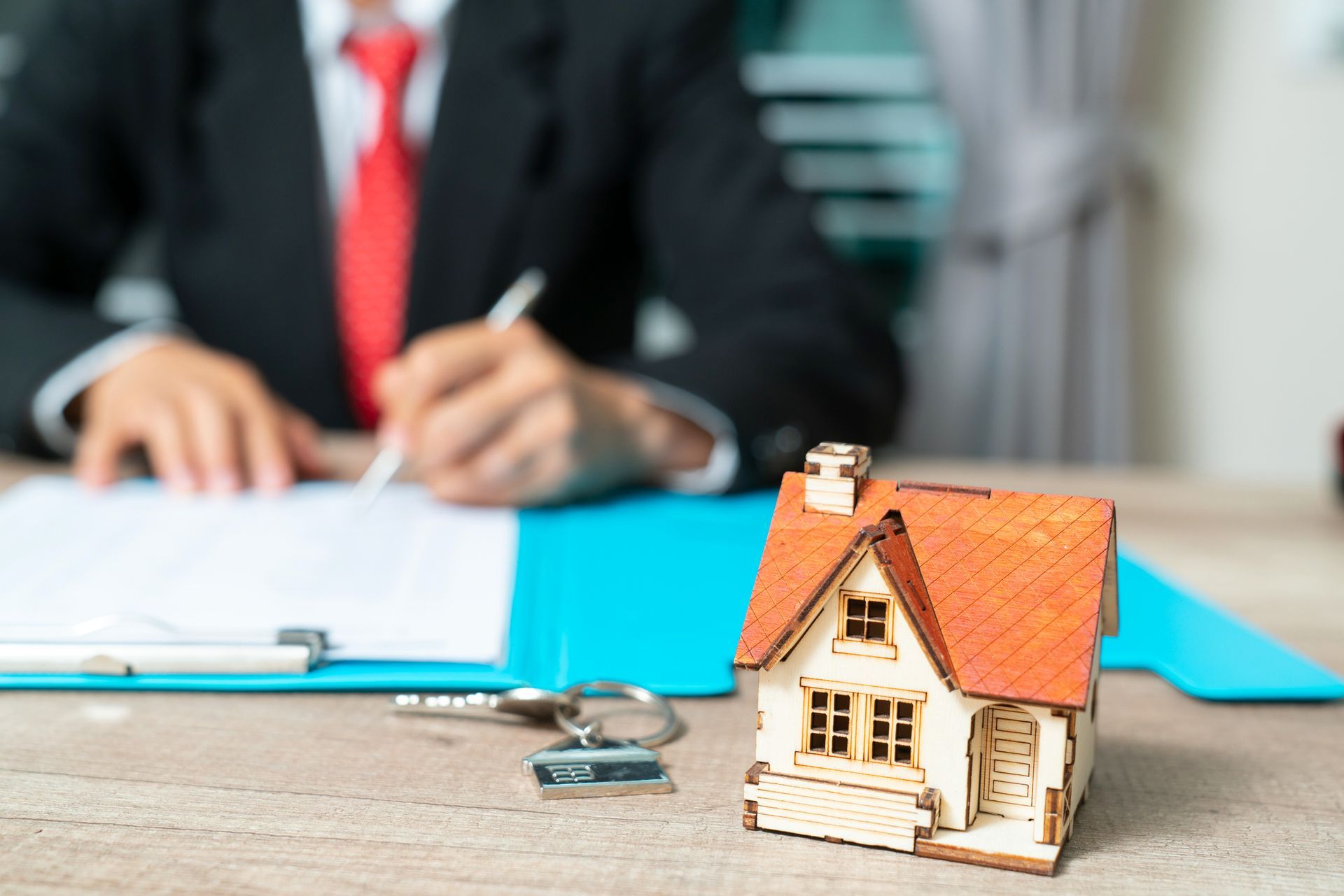 A man in a suit and tie is signing a document next to a model house.