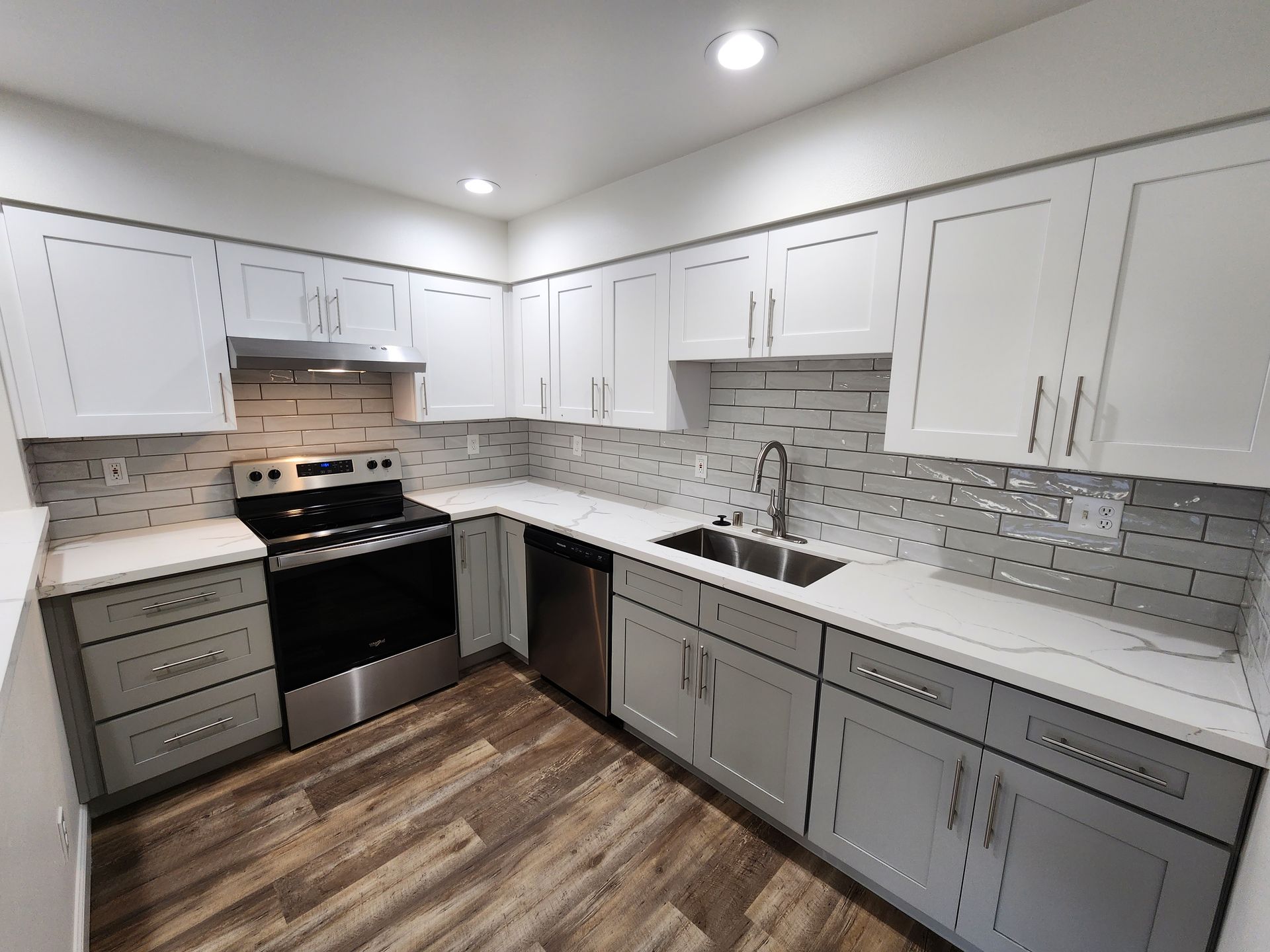 Modern kitchen with gray and white cabinets, stainless steel appliances, and wood-look flooring.