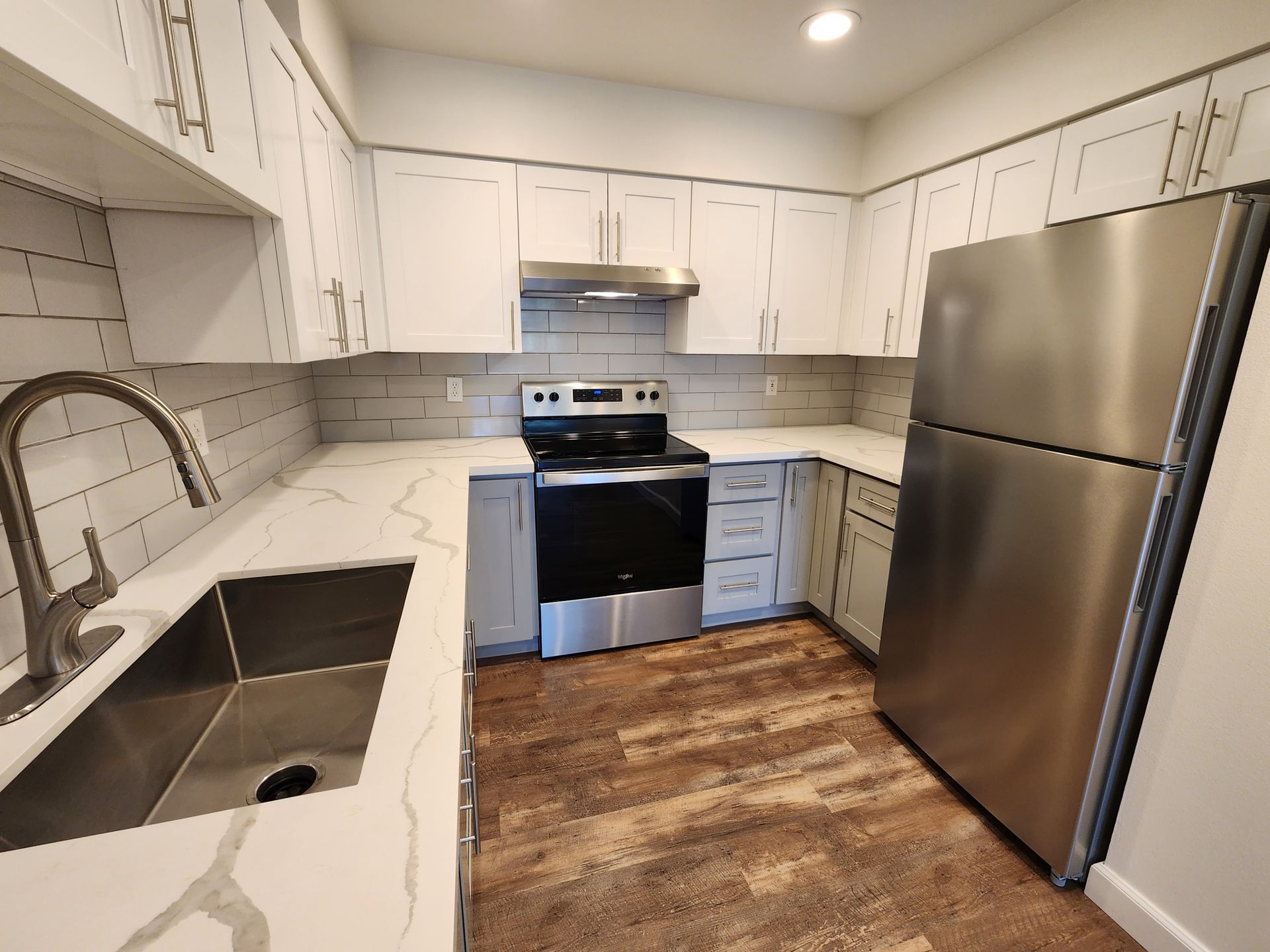 Modern kitchen with white cabinets, stainless steel appliances, and wood-look flooring.