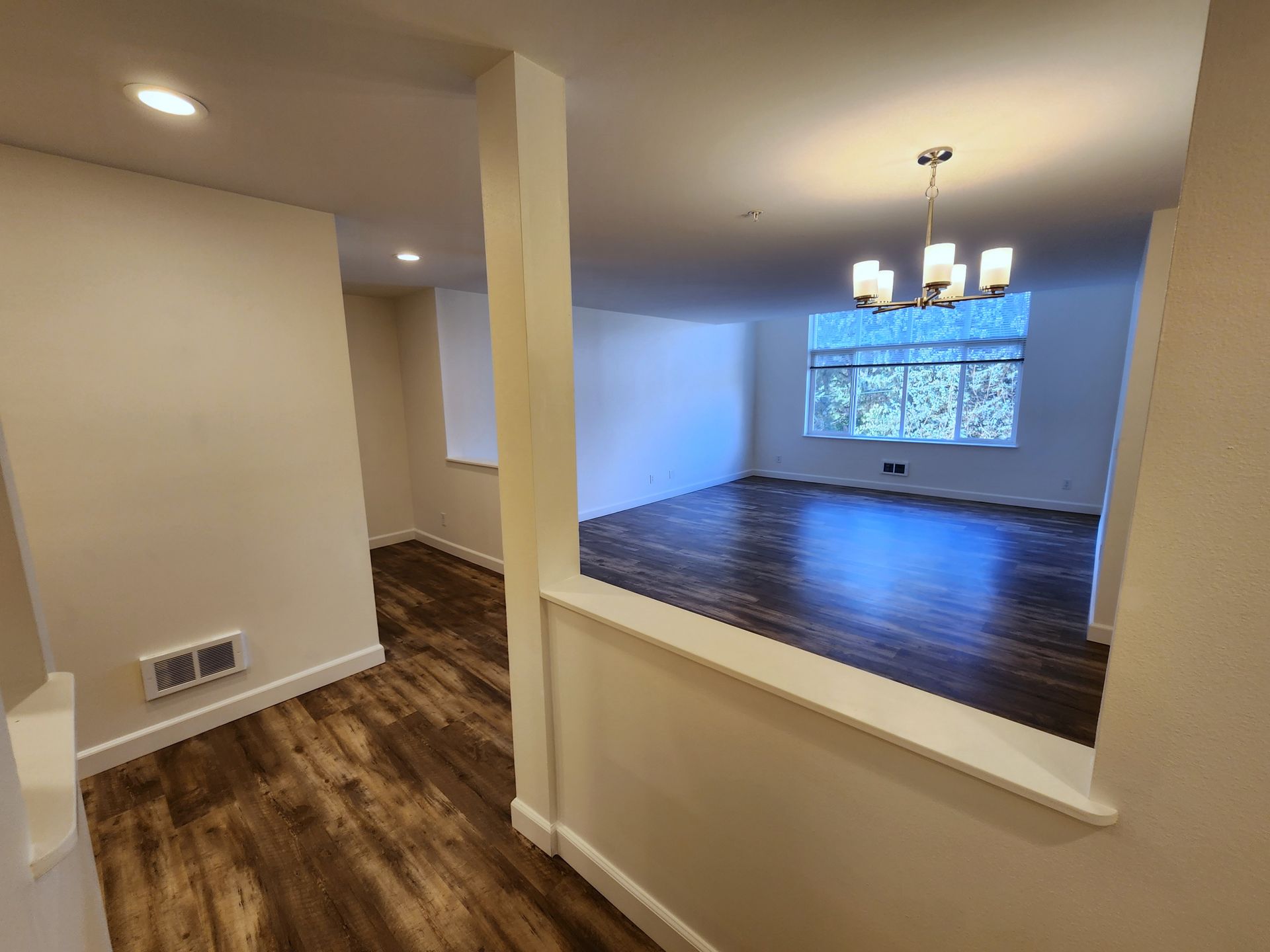 Interior view of a newly renovated home. Dark wood floors, white walls, and a chandelier in the living room.