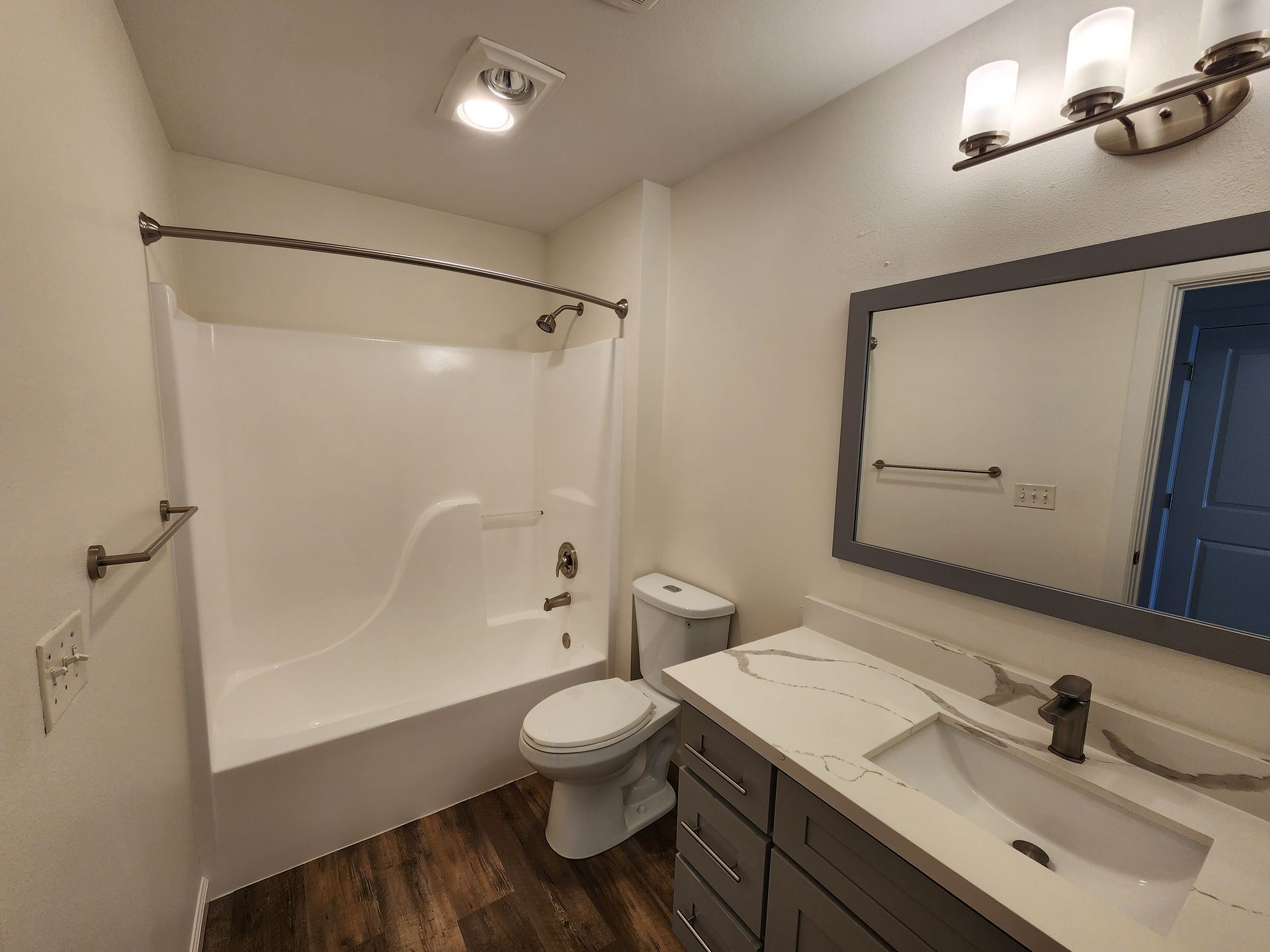 Bathroom with a white bathtub and sink, gray vanity, toilet, and a mirror with a gray frame.