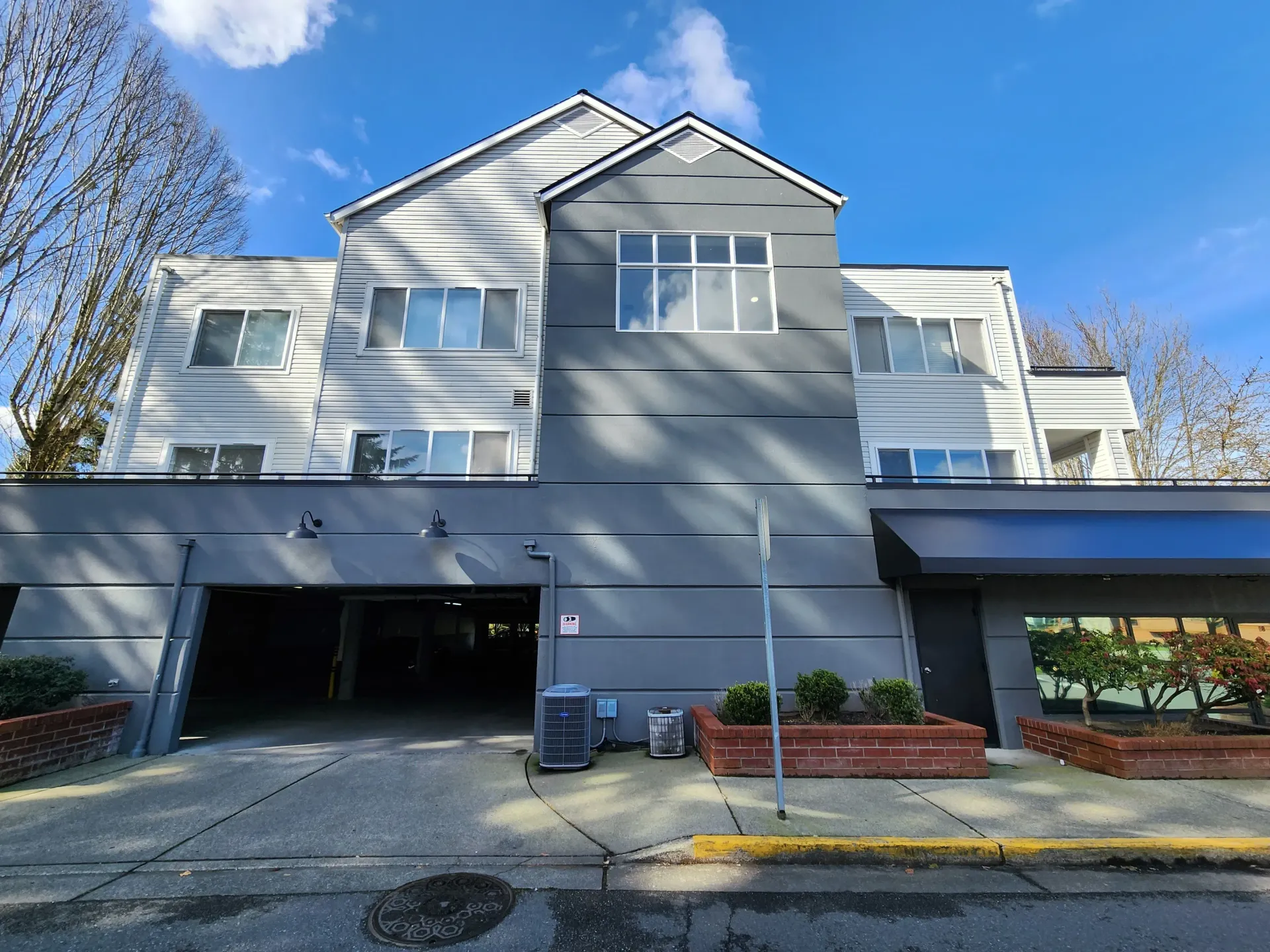 Apartment building exterior, gray and white facade, parking garage entrance, clear blue sky.