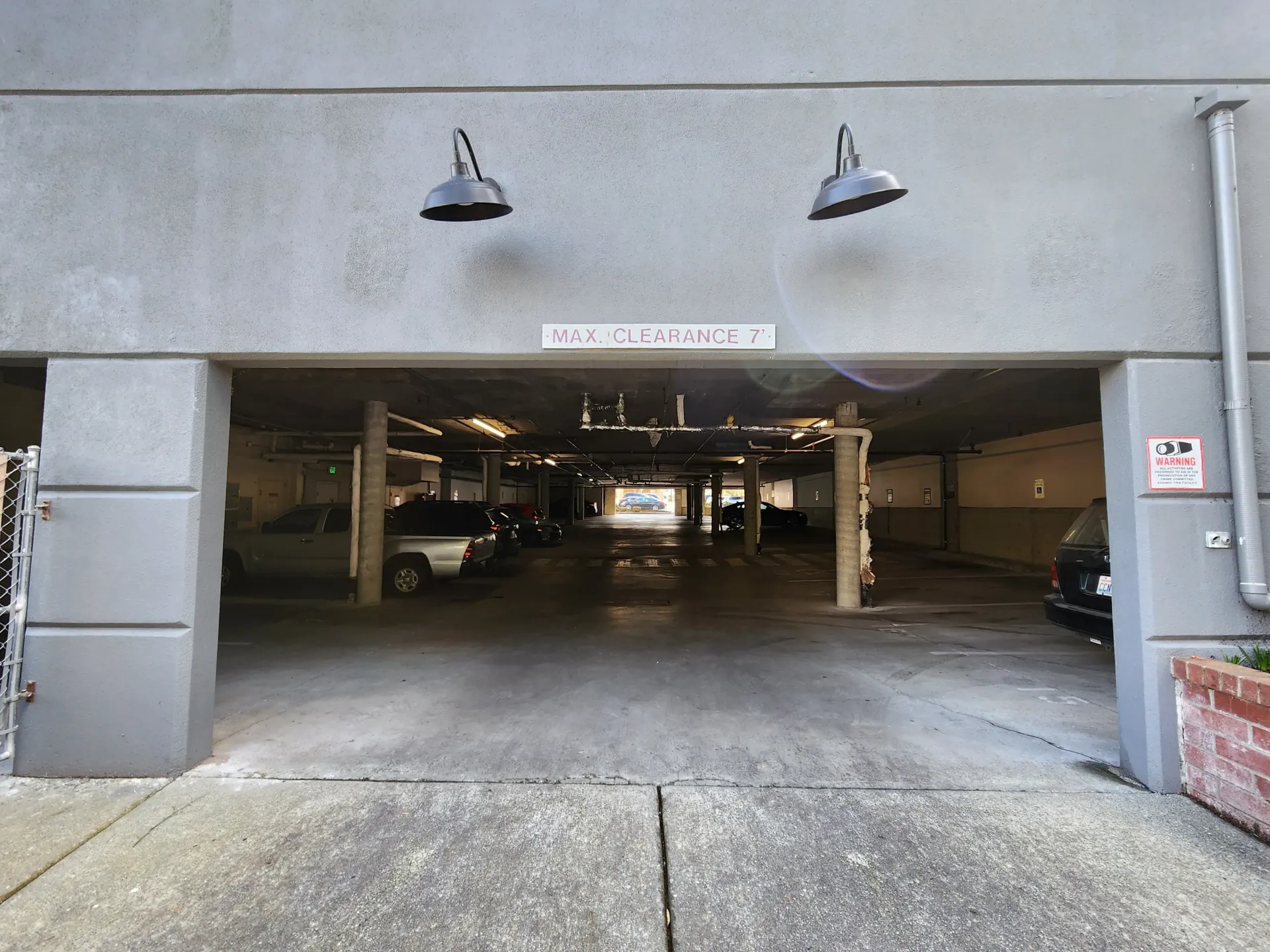 Entrance to a parking garage with clearance sign, overhead lights, and parked cars. Concrete structure.