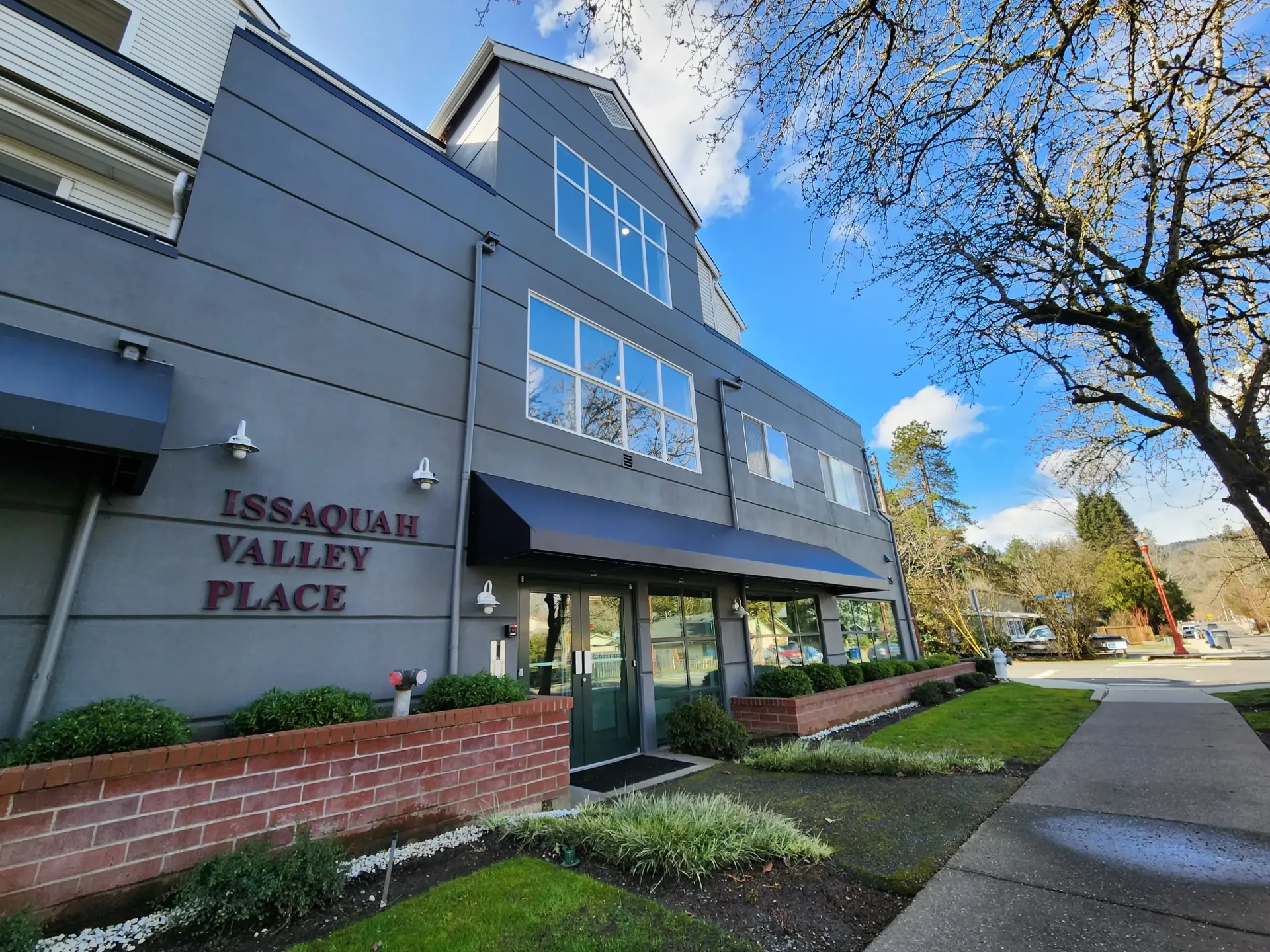 Issaquah Valley Place building with dark gray exterior, black awnings, and glass door entry, under a bright blue sky.