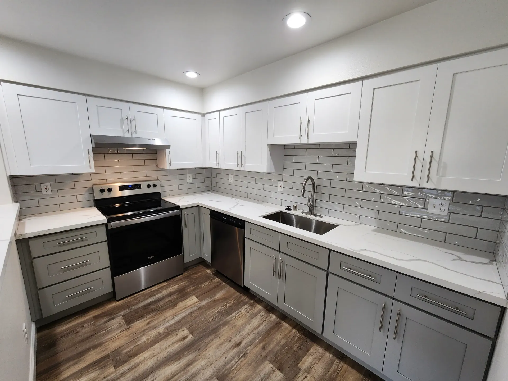 Modern kitchen with white and gray cabinets, stainless steel appliances, and wood-look flooring.