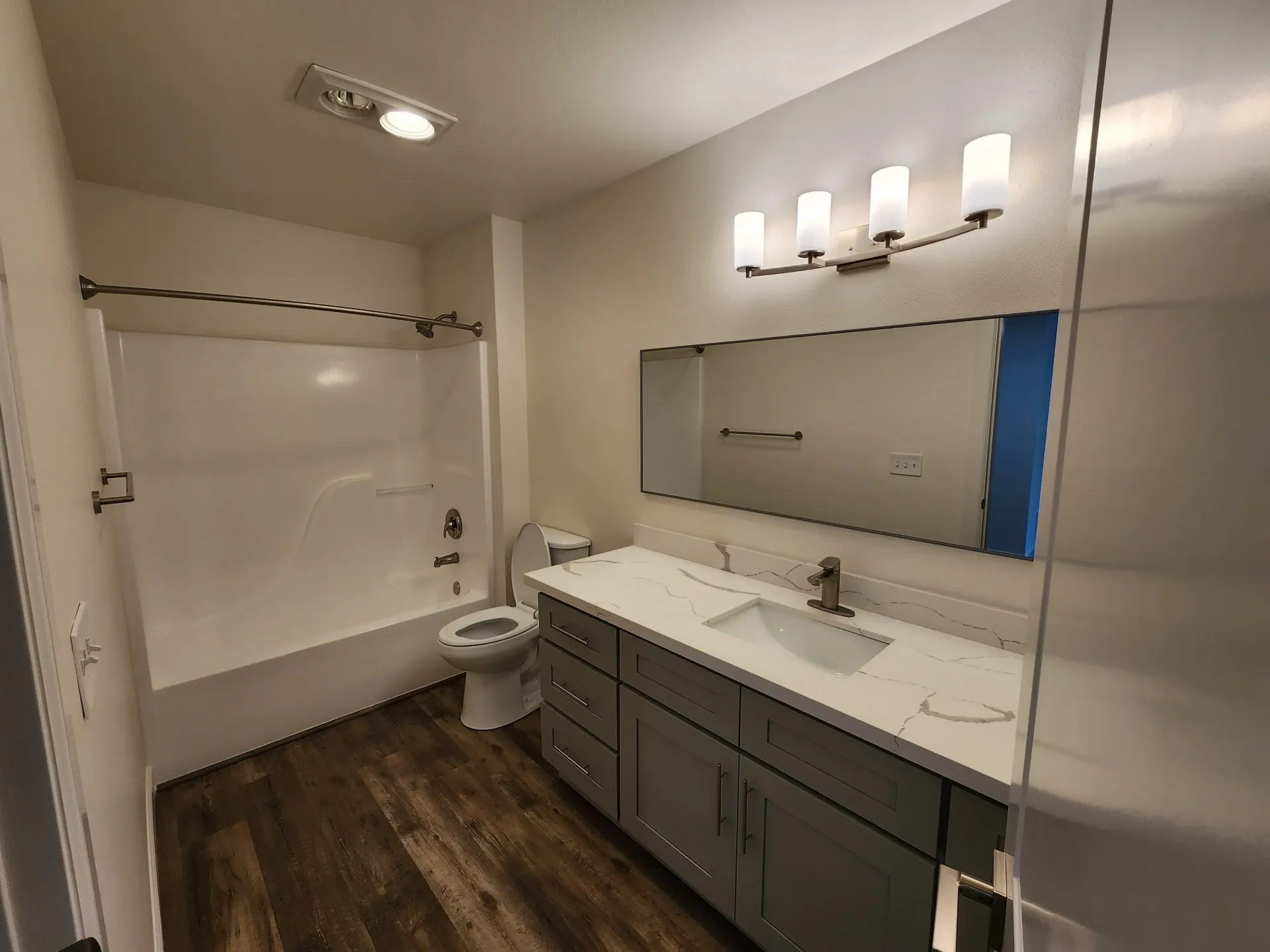 Bathroom with a gray vanity, white countertop, and a shower/tub combo with wood-look flooring.