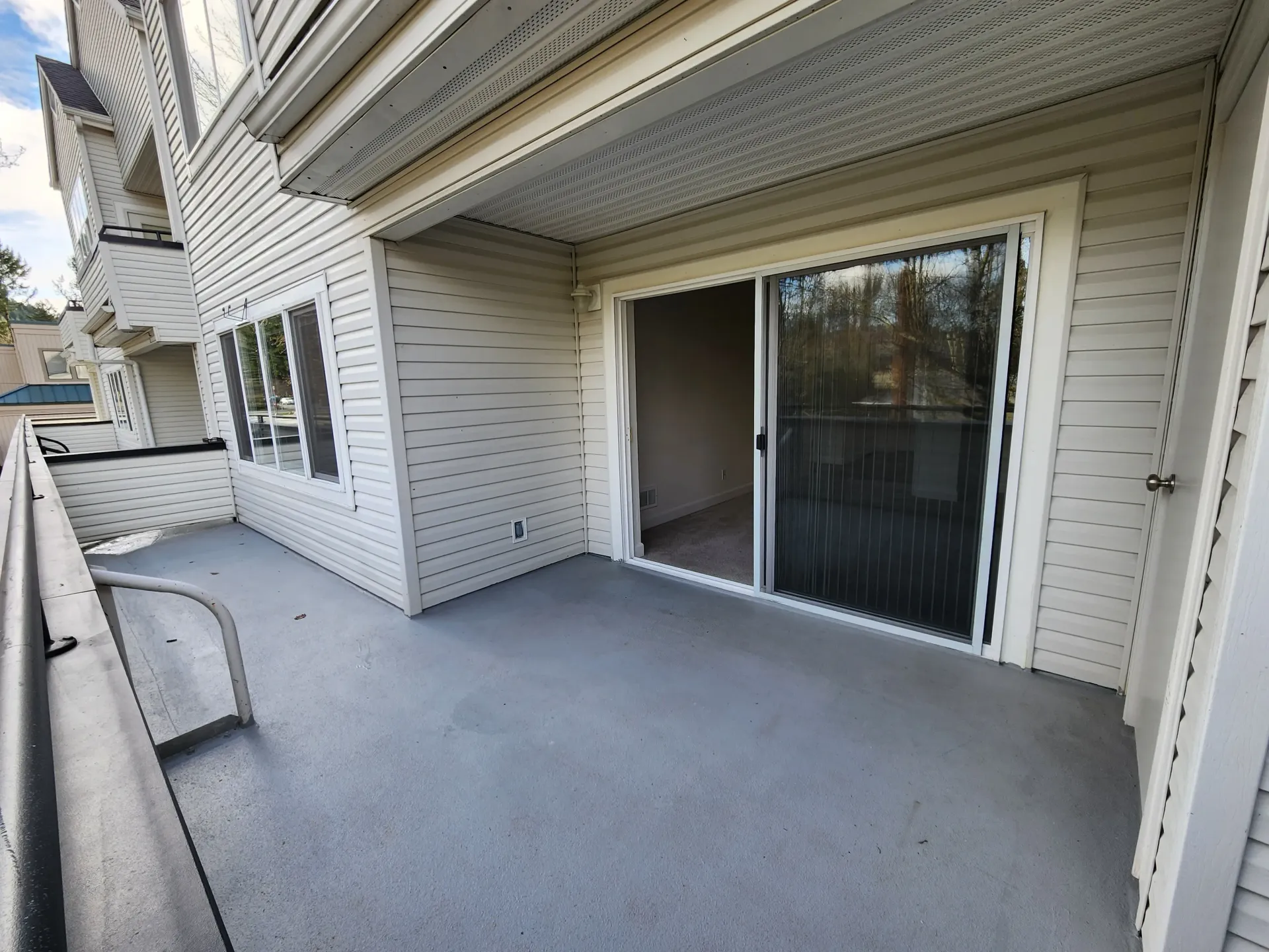 A gray balcony with a sliding glass door. The exterior has beige siding and a metal railing.