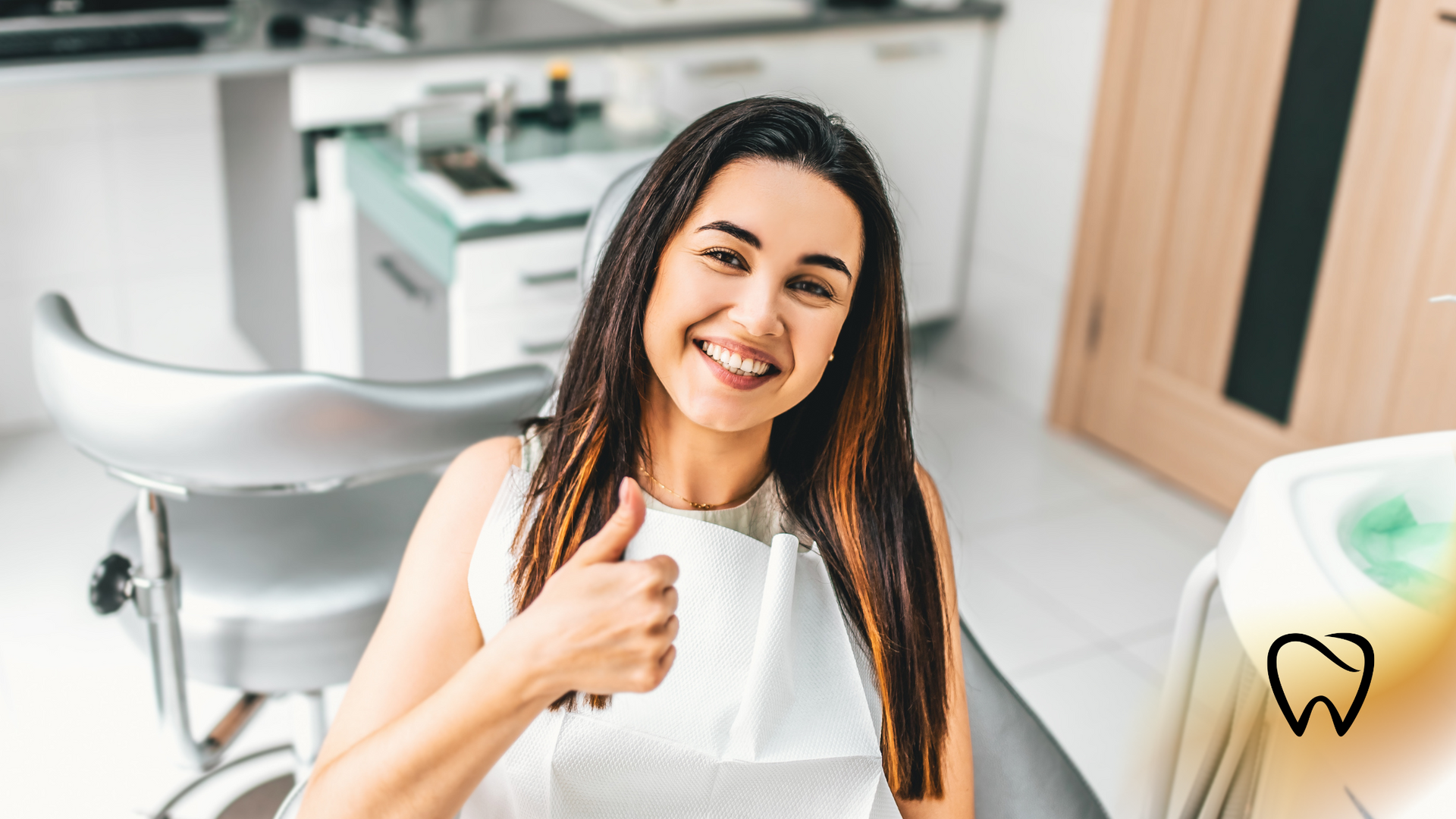 Woman in dentist chair gives thumbs up, smiling.