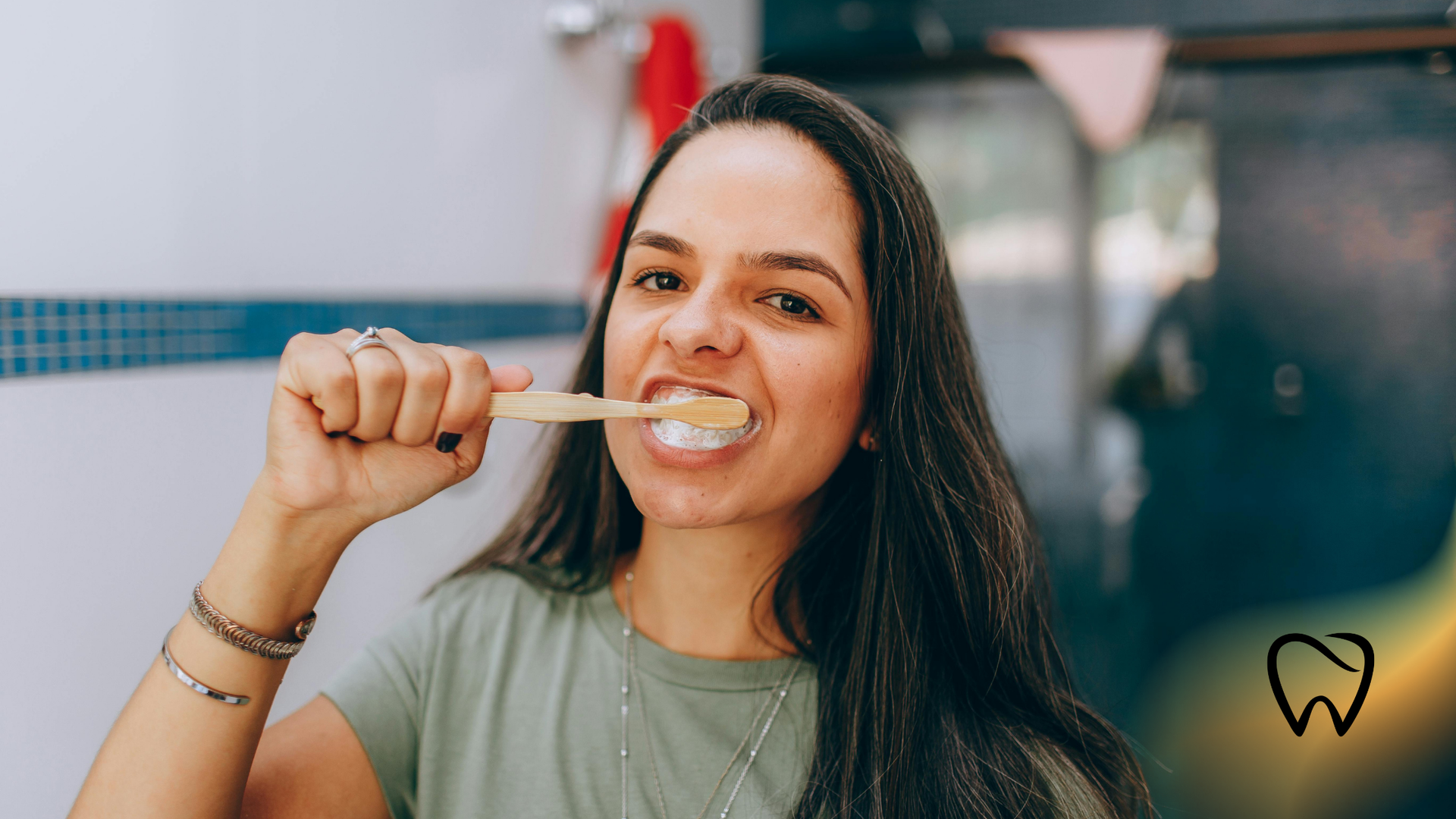 Woman brushing teeth in a bathroom, smiling, holding a wooden toothbrush.